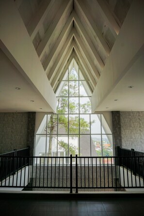 A spacious interior with a high ceiling, large windows, and a view of trees and buildings outside. - Are You And I Bed & Breakfast (Bandung)