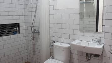 A bathroom with white tiled walls, a white toilet, a sink with a mirror above it, and a shower area.