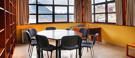 A conference room with a large table and chairs, large windows with a mountain view, and a wooden bookshelf.