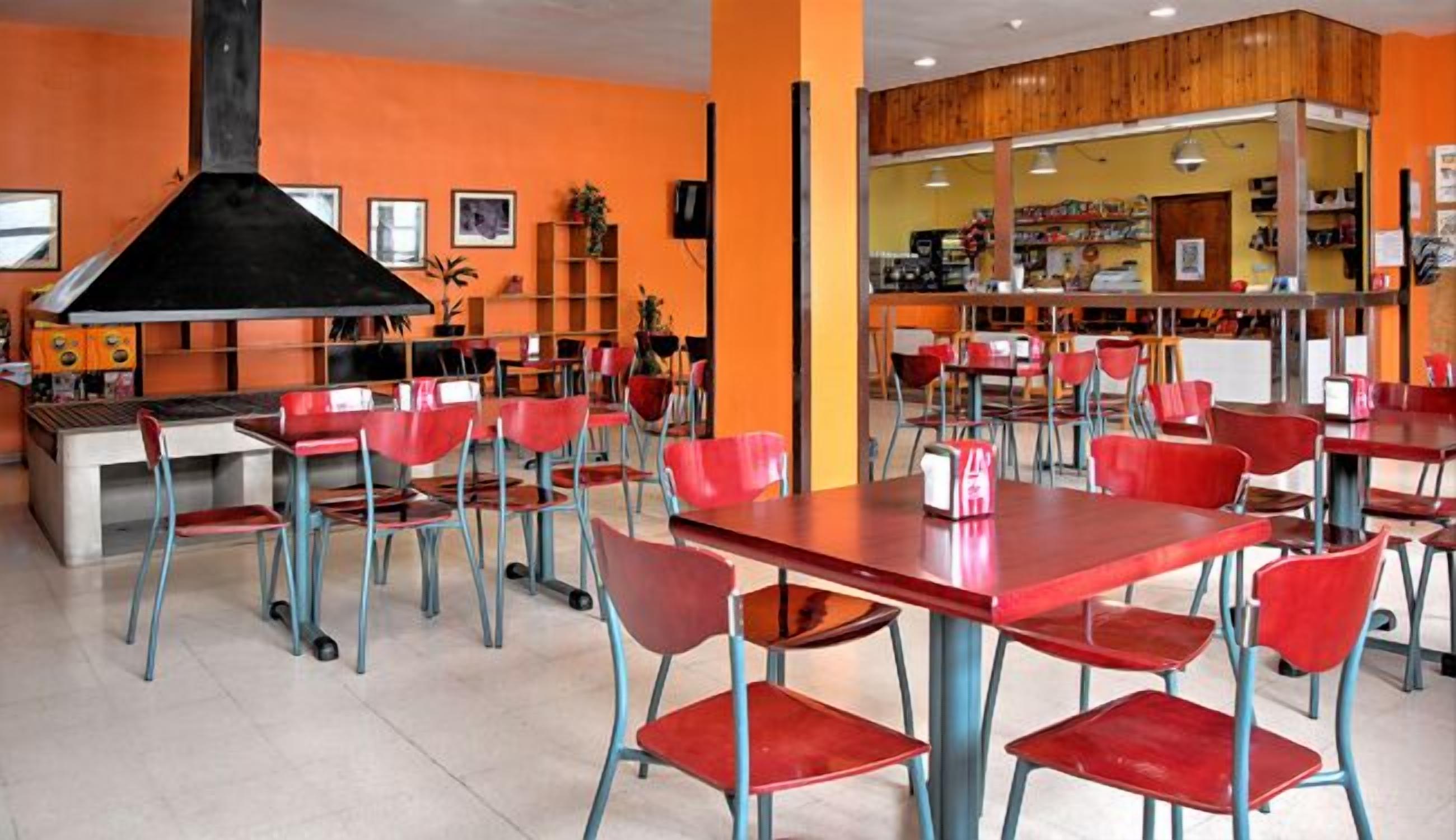 Een restaurant met rode stoelen en tafels, een zwarte grill en oranje wanden.