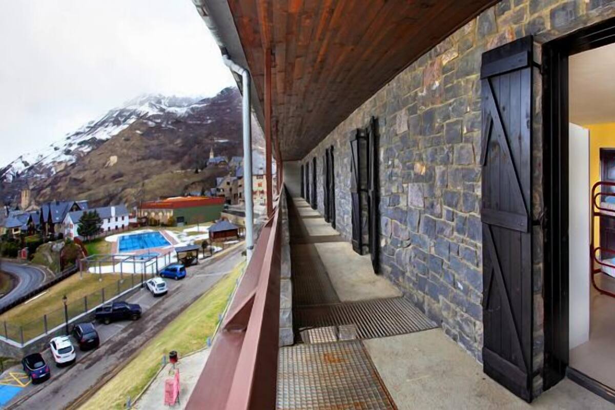 A hotel balcony with stone walls, a pool, and a view of a mountainous area.