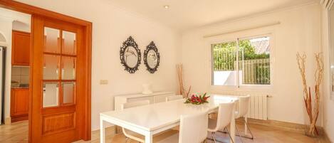 A dining area with a white table and chairs, a wooden door, and two wall-mounted mirrors.
