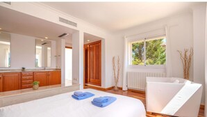 Ein Hotelzimmer mit einem großen Bett, einem weißen Sofa, einem Fenster mit Blick auf Bäume und Holzboden.