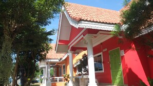 Un bâtiment rouge avec un toit en tuiles, des colonnes blanches et une porte verte.