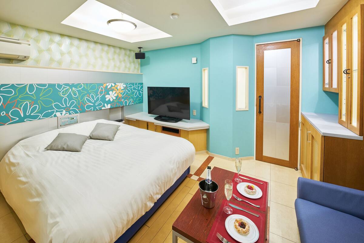 Ein Hotelzimmer mit Bett, Fernseher, Esstisch mit Tellern und Gläsern sowie einem Holzschrank.