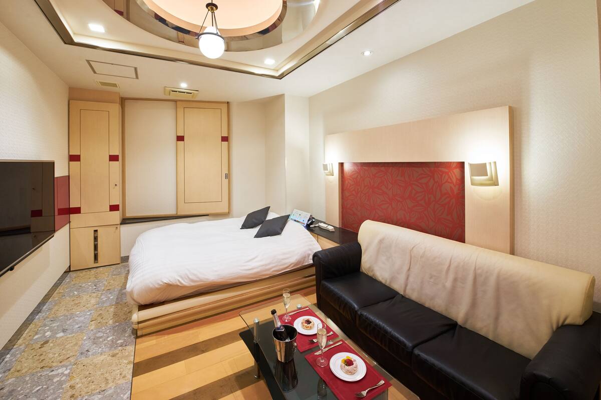 Ein modernes Hotelzimmer mit einem Bett, einer schwarzen Ledersofa, einem kleinen Tisch mit einer roten Unterlage und einem Fernseher.