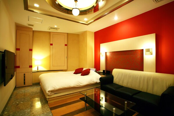 A hotel room with a bed, a sofa, a glass coffee table, and a TV.