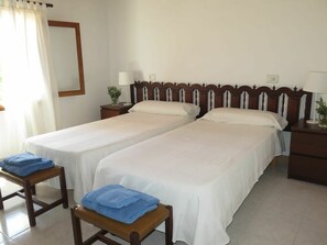 Une chambre d’hôtel avec deux lits simples, une tête de lit en bois, des tables de chevet avec des lampes et une chaise avec des serviettes.