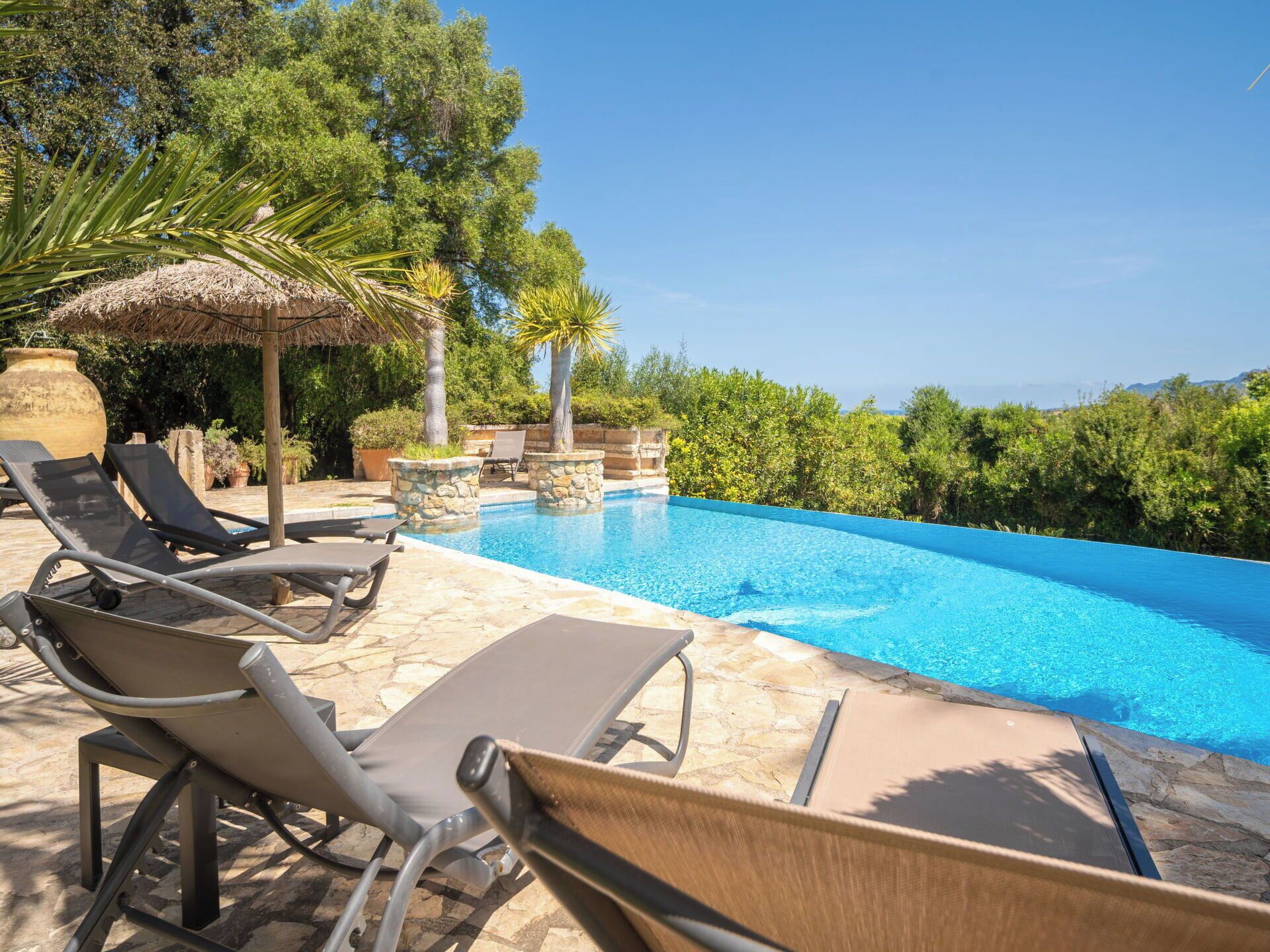 Une piscine entourée de chaises longues, une structure en pierre et une vue sur la mer.
