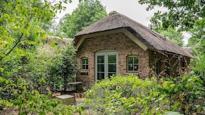 A rustic brick house with a thatched roof, surrounded by lush greenery. - Vlindervallei Studio 2p (Ermelo)