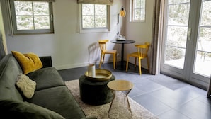A living room with a sofa, two chairs, a small table, and a window with curtains. - Vlindervallei Studio 2p (Ermelo)
