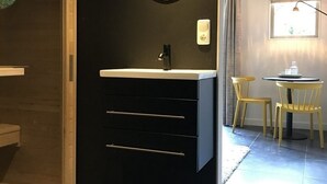A modern bathroom with a black vanity, a round mirror, and a small table with chairs. - Vlindervallei Studio 2p (Ermelo)