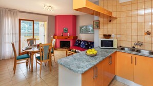 Une cuisine moderne avec des meubles de couleur orange, un plan de travail en marbre et un coin repas comprenant des chaises et une table en bois.