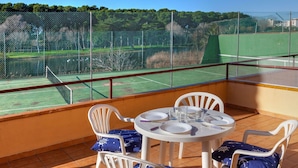 Un balcon donnant sur un court de tennis, avec des chaises blanches et une table dressée pour deux personnes.