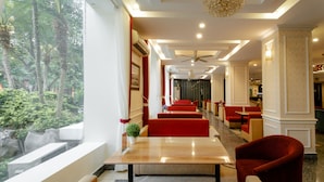A hotel lobby with red seating, a long table, and a view of greenery outside.