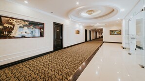 A hotel corridor with a patterned carpet, framed artwork on the walls, and a modern ceiling design.