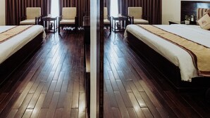 A hotel room with two beds, a large mirror, wooden flooring, and a view of the outdoors.