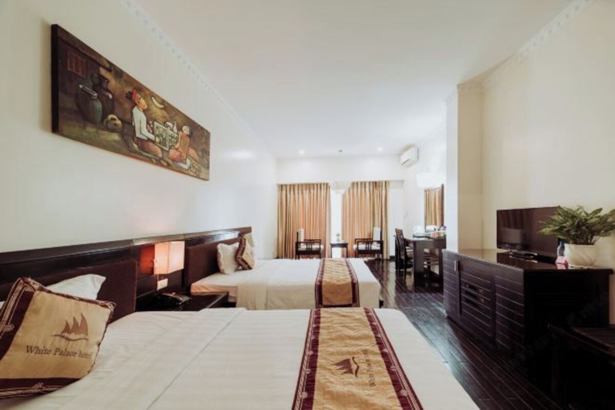 A hotel room with two beds, a desk, a television, and a painting on the wall.