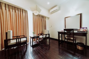 Habitación de hotel con piso de madera, un escritorio con silla, un sofá, una lámpara y un espejo grande.