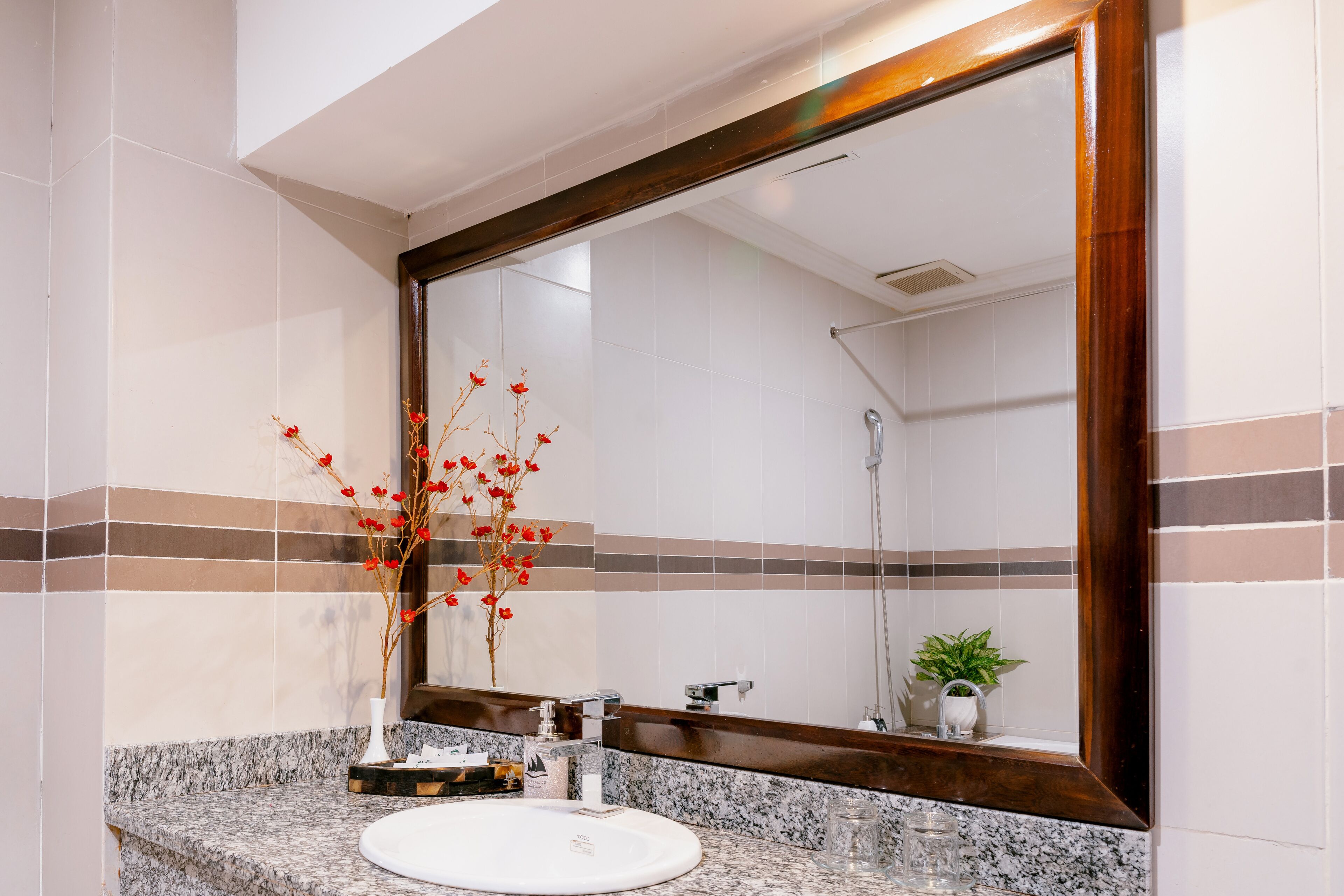 Ein Badezimmer mit einem weißen Waschbecken, einem Spiegel und einer Vase mit roten Blumen.
