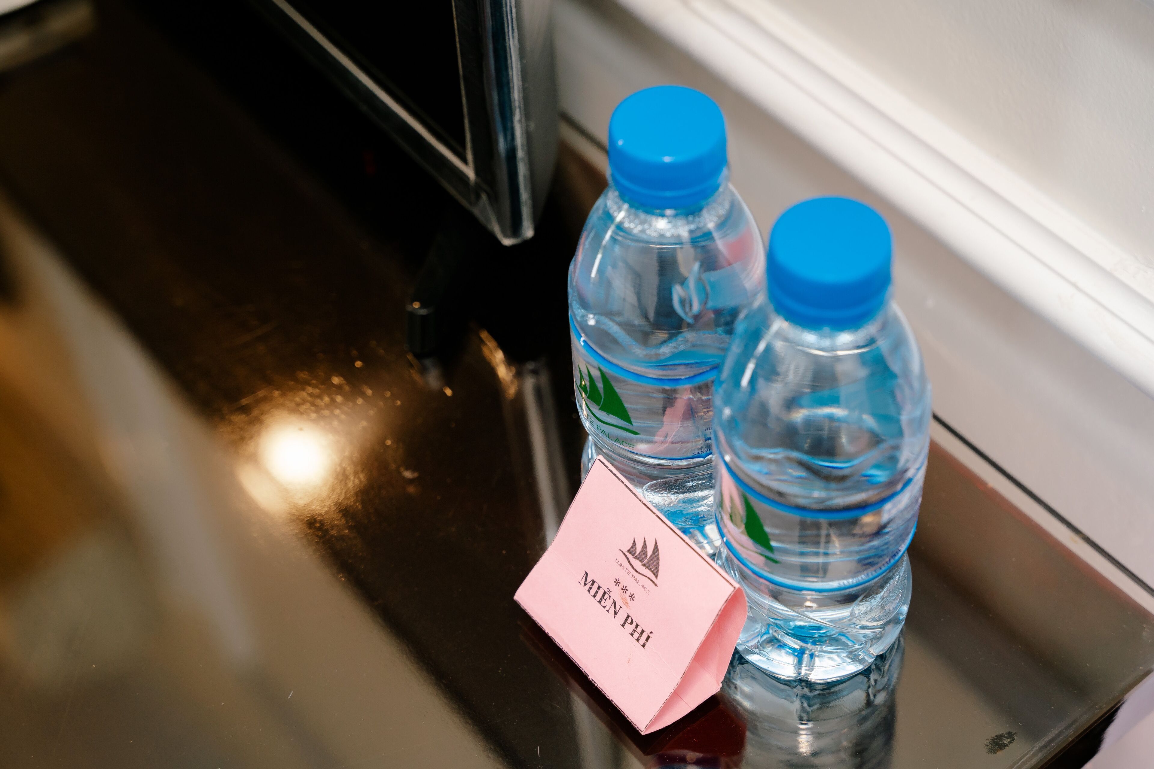Dos botellas de agua y una tarjeta rosa sobre una superficie reflectante.