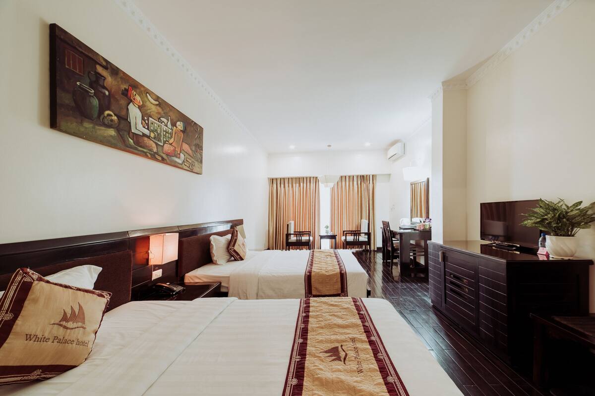 A hotel room with two beds, a painting on the wall, a desk with a chair, and a TV on a dresser.