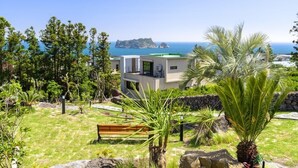 Une villa moderne offrant une vue sur la mer et dotée d’un jardin rocheux agrémenté d’un banc.