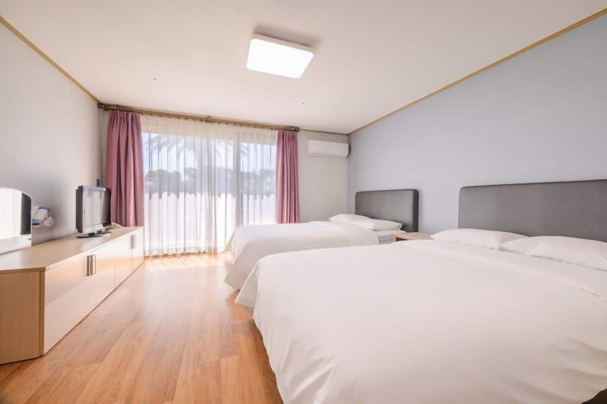 A hotel room with two beds, a desk with a TV, and a window with curtains.