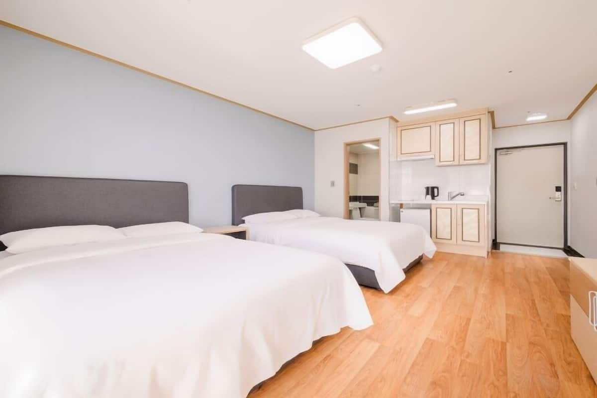 A hotel room with two beds, a kitchenette, and a bathroom.