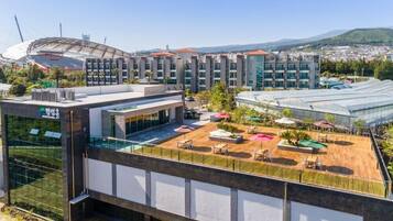 A hotel with a rooftop pool area, a large sports stadium in the background, and a view of a cityscape with mountains.
