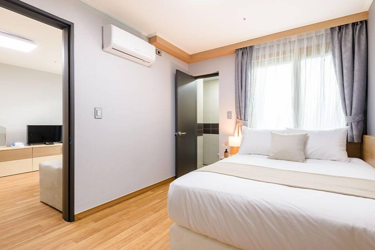 A modern hotel room with a bed, a desk, and an air conditioning unit.