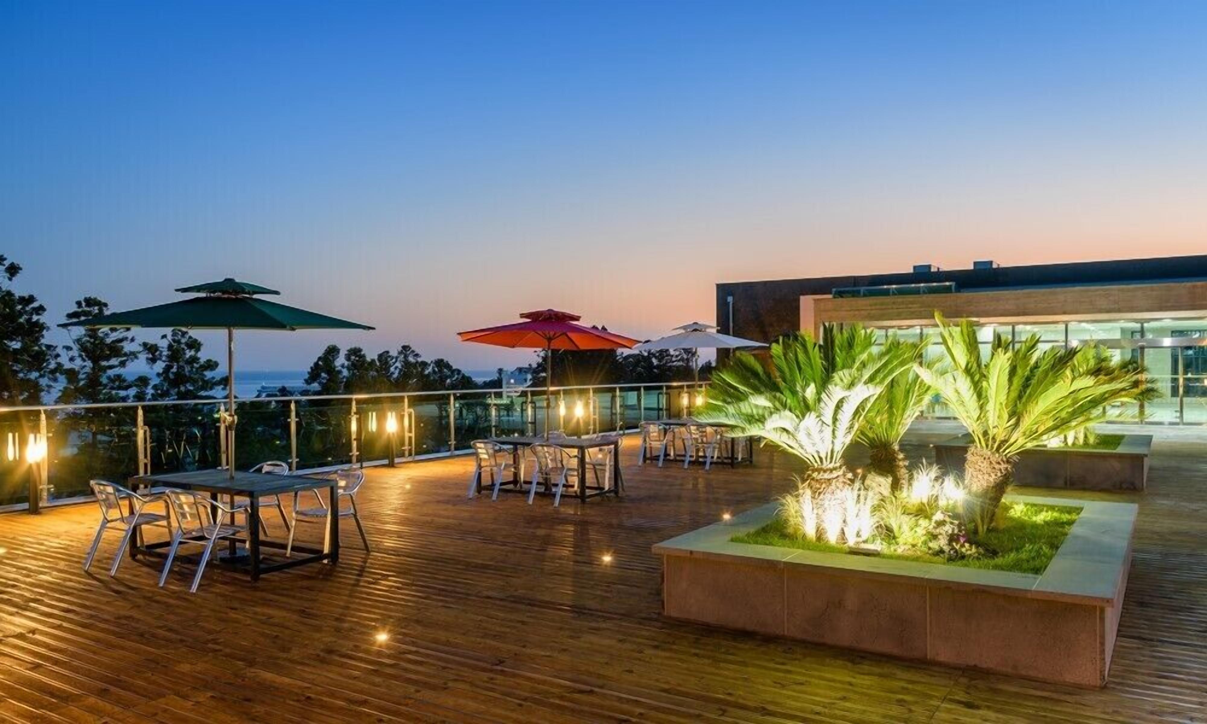 An outdoor terrace with wooden flooring, tables, chairs, and umbrellas.