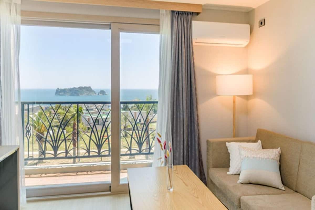 A hotel room with a balcony, a sofa, a table, and a lamp.