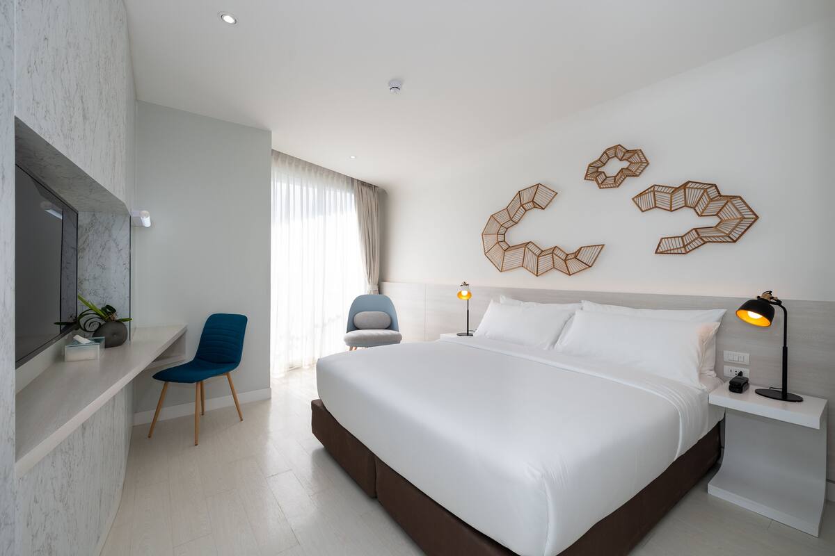 Una habitación de hotel moderna con una cama grande, un escritorio, una silla y detalles decorativos en la pared.