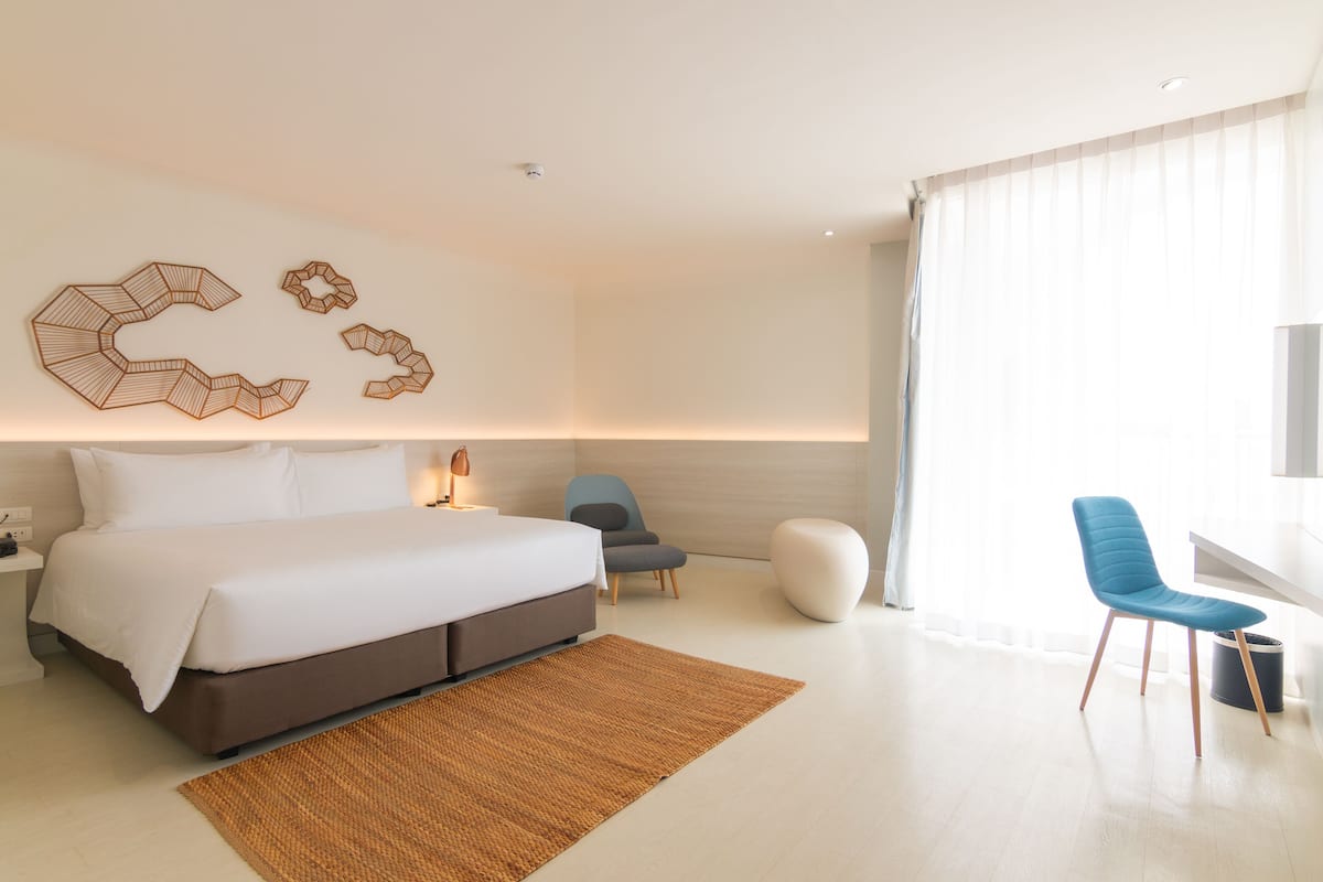 Una habitación de hotel moderna con una cama grande, un escritorio, dos sillas y una obra de arte en la pared.