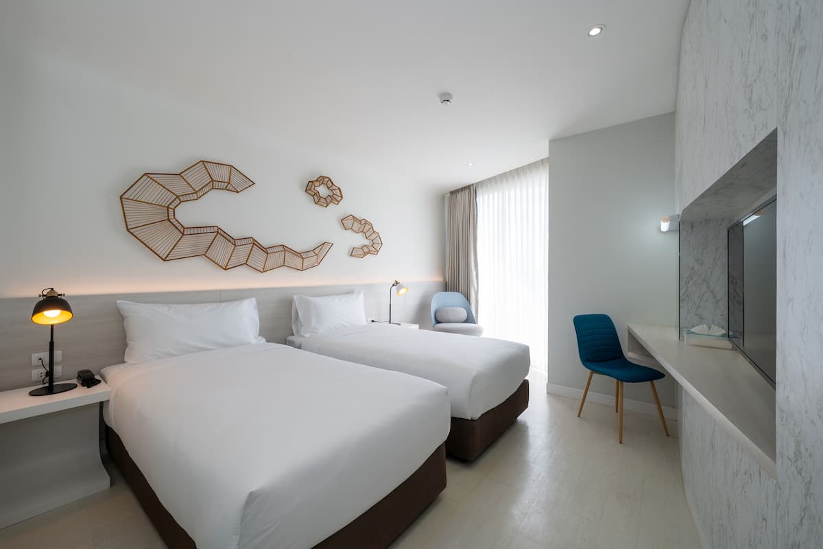 Habitación de hotel con dos camas, un escritorio con lámpara, una silla, televisión y decoración en la pared.
