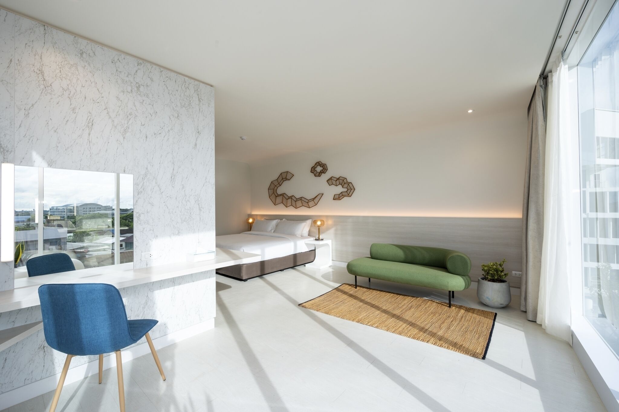 A modern bedroom with a bed, a green sofa, a blue chair, and a large window.