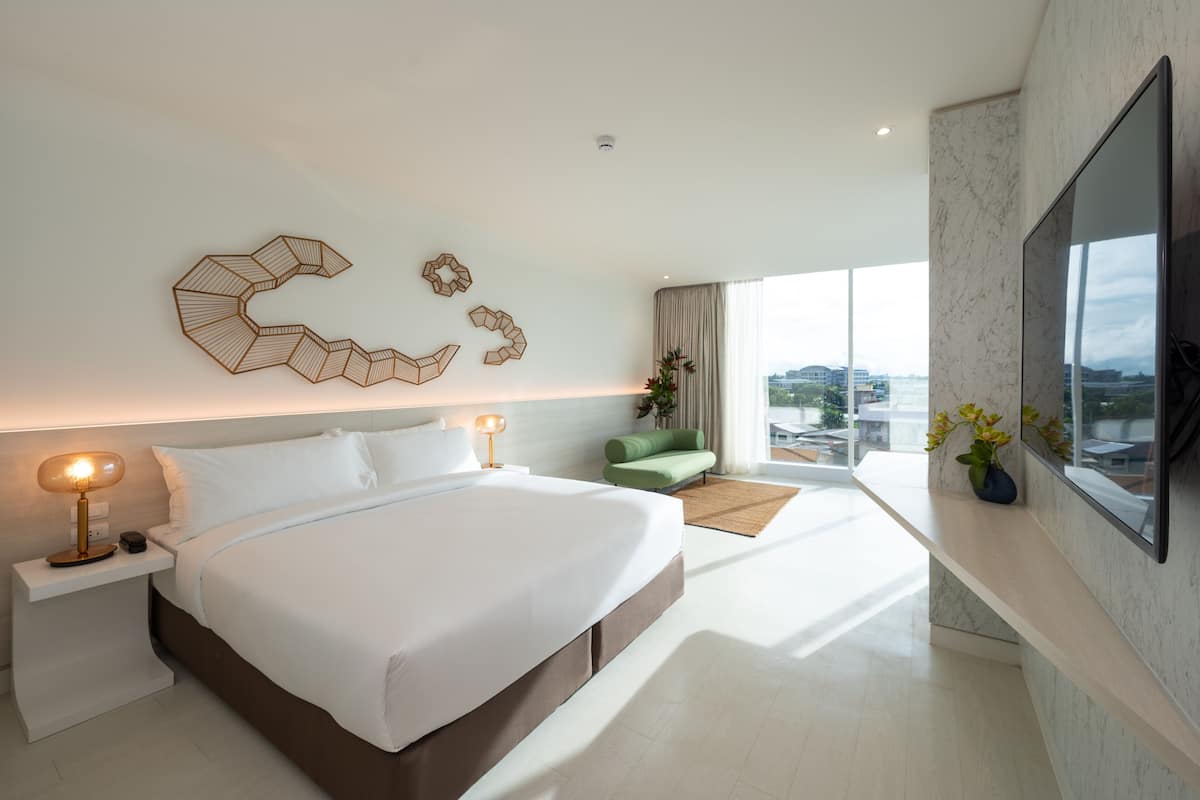 Una habitación de hotel moderna con una cama grande, un televisor de pantalla plana, un sofá verde y vistas a la ciudad.