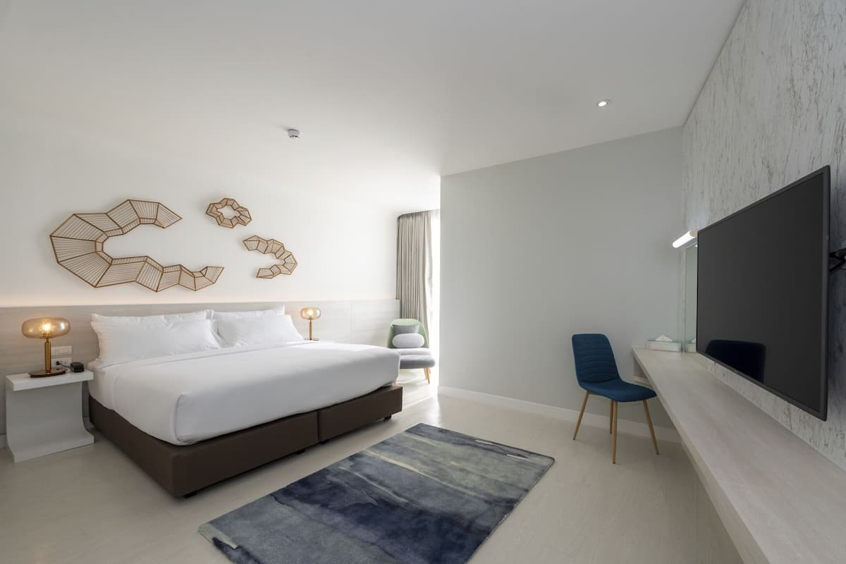 Un dormitorio moderno con una cama grande, mesitas de noche, un televisor de pantalla plana y un rincón de estar con una silla.
