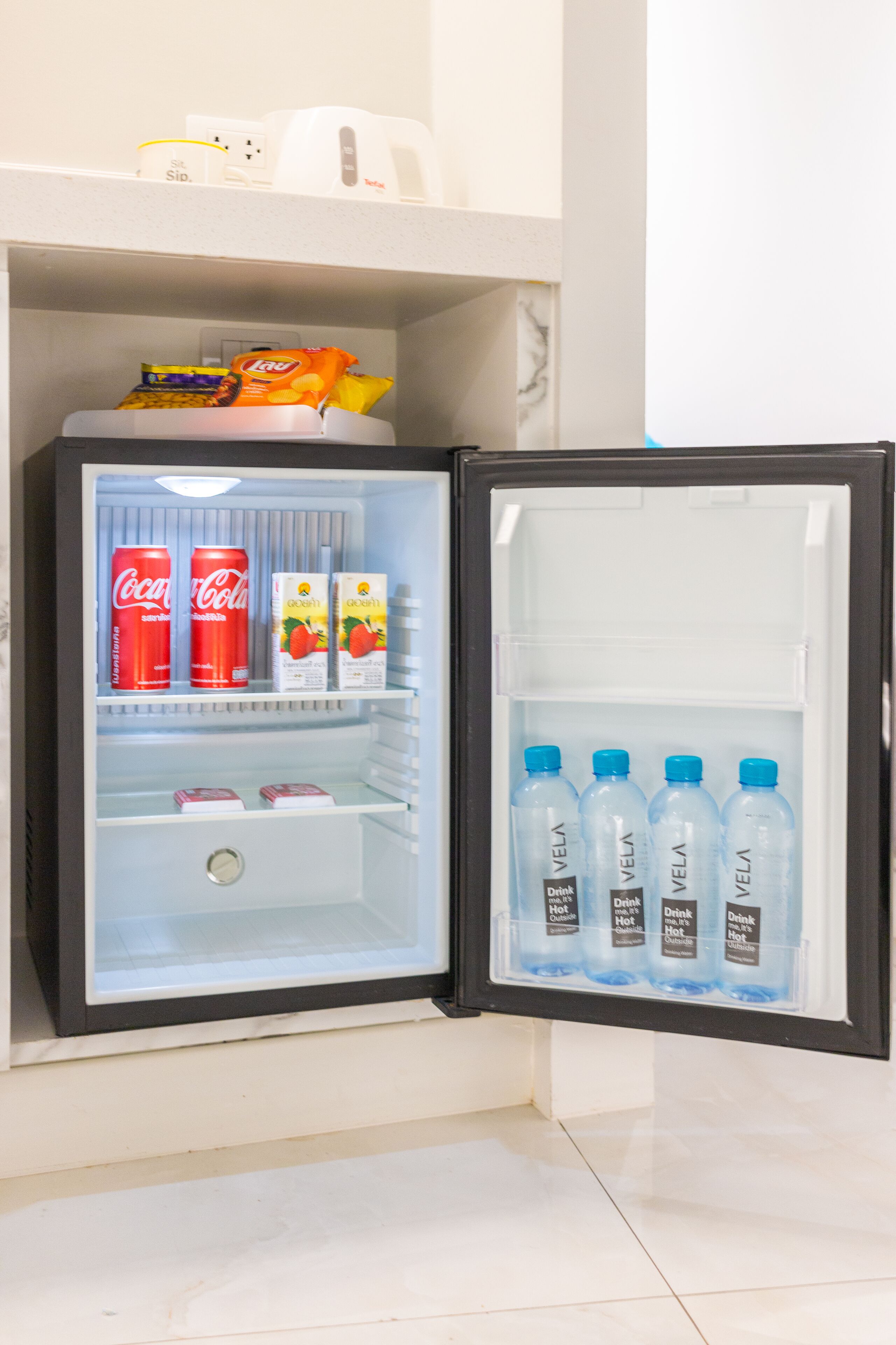 A mini-fridge with Coca-Cola cans, juice boxes, and water bottles.