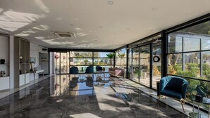 A spacious, modern interior with a polished marble floor, large windows offering a view of a pool and greenery, and contemporary furniture. - Leaf Port Hotel (Konyaalti)