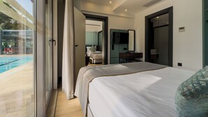 A modern hotel room with a large bed, a desk, a chair, a TV, and a view of a swimming pool. - Leaf Port Hotel (Konyaalti)