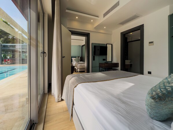 Una habitación de hotel moderna con una cama grande, un escritorio, una silla, un televisor y vistas a una piscina.