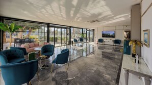 A modern interior with a glass wall, teal chairs, a pink sofa, and a marble floor. - Leaf Port Hotel (Konyaalti)