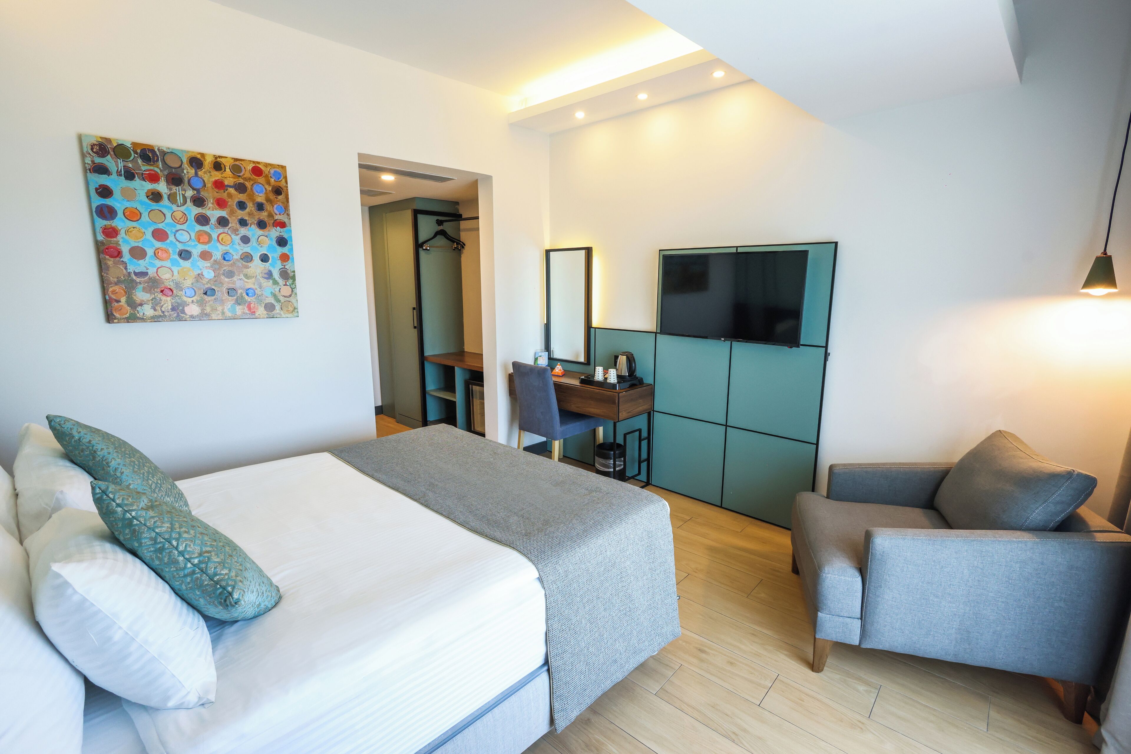 A modern hotel room with a bed, two chairs, a desk, and a TV.