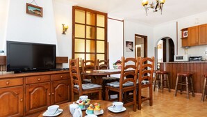 A dining area with wooden furniture, a television, and a kitchen area with wooden cabinets and a microwave.