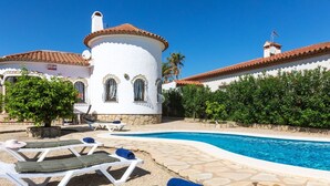 A poolside area with lounge chairs, a swimming pool, and a building with a tiled roof and white walls.