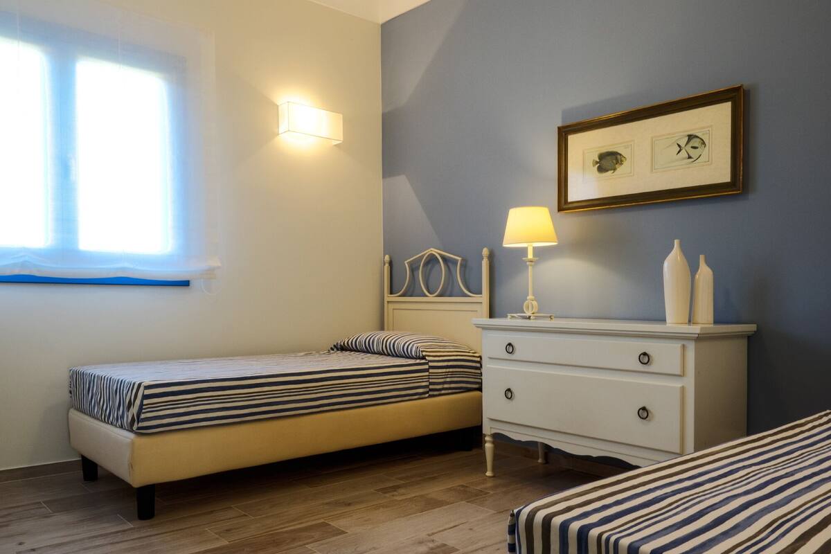 A bedroom with two beds, a dresser, a nightstand, and a window with curtains.