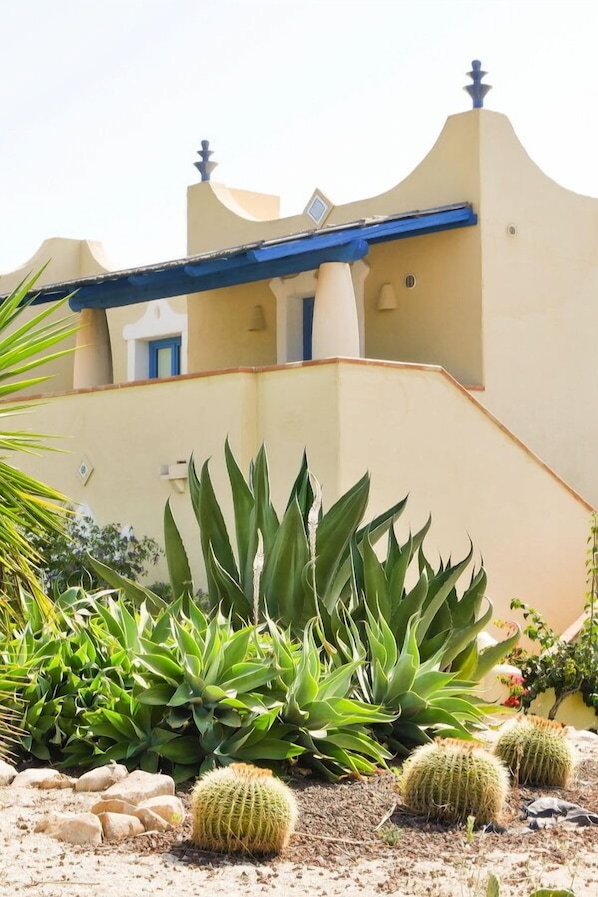 A building with a beige facade and blue accents, surrounded by cacti and agave plants. - Marsa Siclà Le Ville (Scicli)