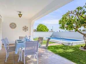 Un patio exterior con mesa de comedor para cuatro personas, piscina y un árbol pequeño.
